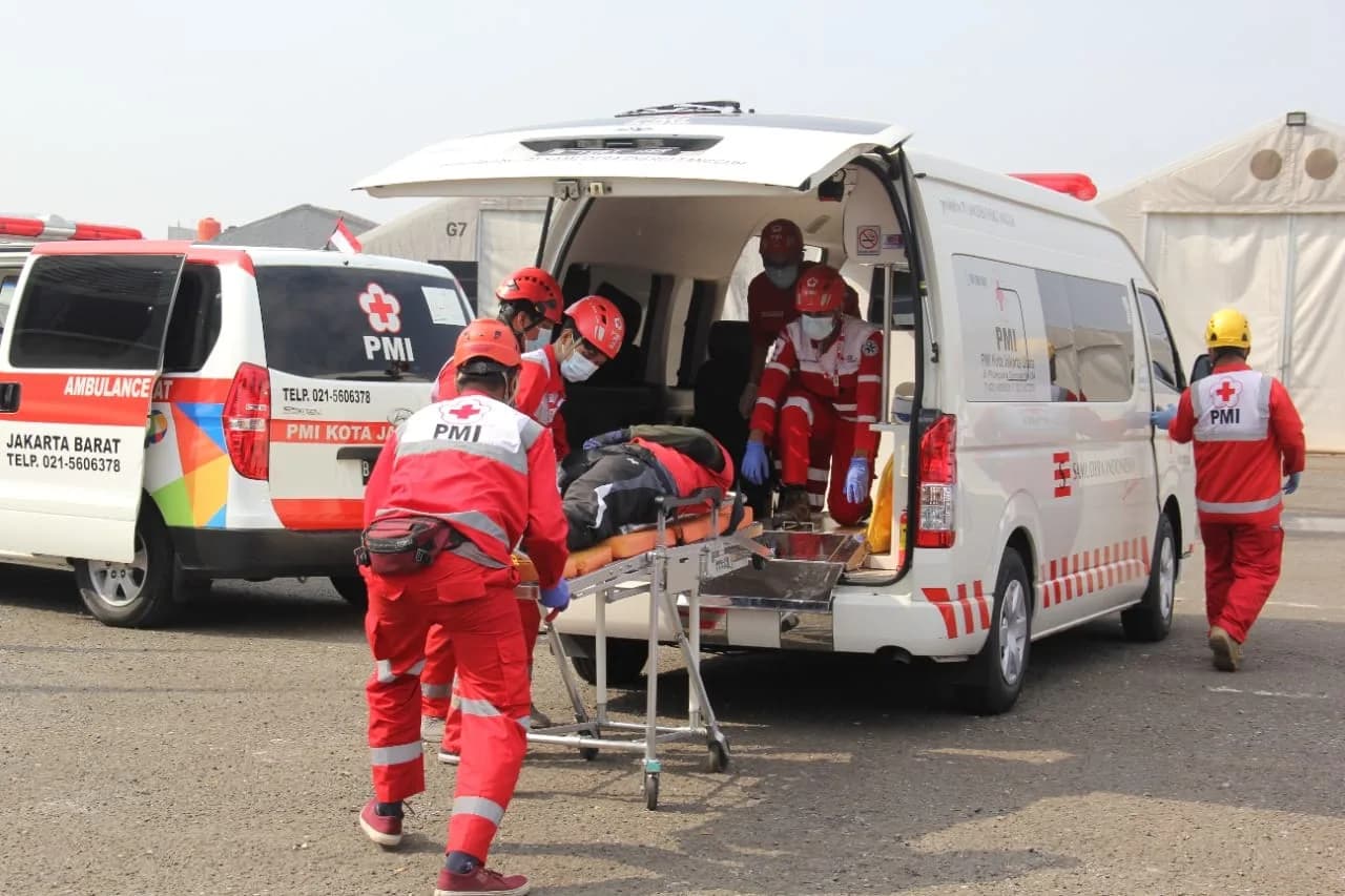 Kru ambulans PMI bersiap memberikan respons gawat darurat di sebuah jalan kota.